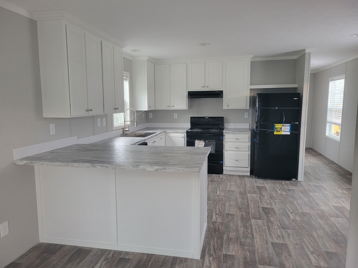 A modern kitchen with white cabinets, marble-patterned countertops, black appliances, and wood-look flooring, creating a clean, spacious feel.