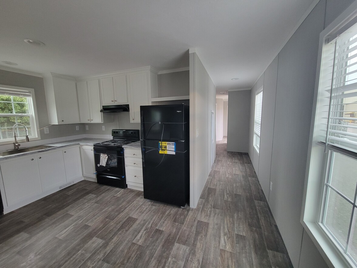 Modern kitchen with white cabinets, black appliances, and wood-look flooring. Bright natural light from windows enhances the clean, minimalist style.