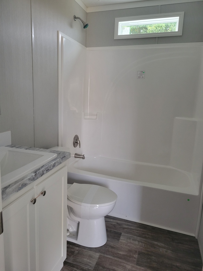 Small bathroom with white fixtures. Features a bathtub with shower, toilet, and a vanity with a marble countertop. A rectangular window provides natural light.