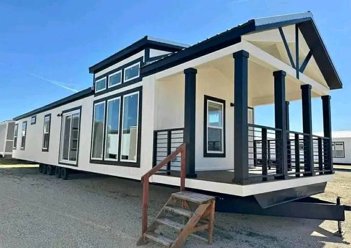 Stylish modern tiny house with large windows and a covered porch. Black accents on white exterior. Blue sky, creating a bright, inviting atmosphere.