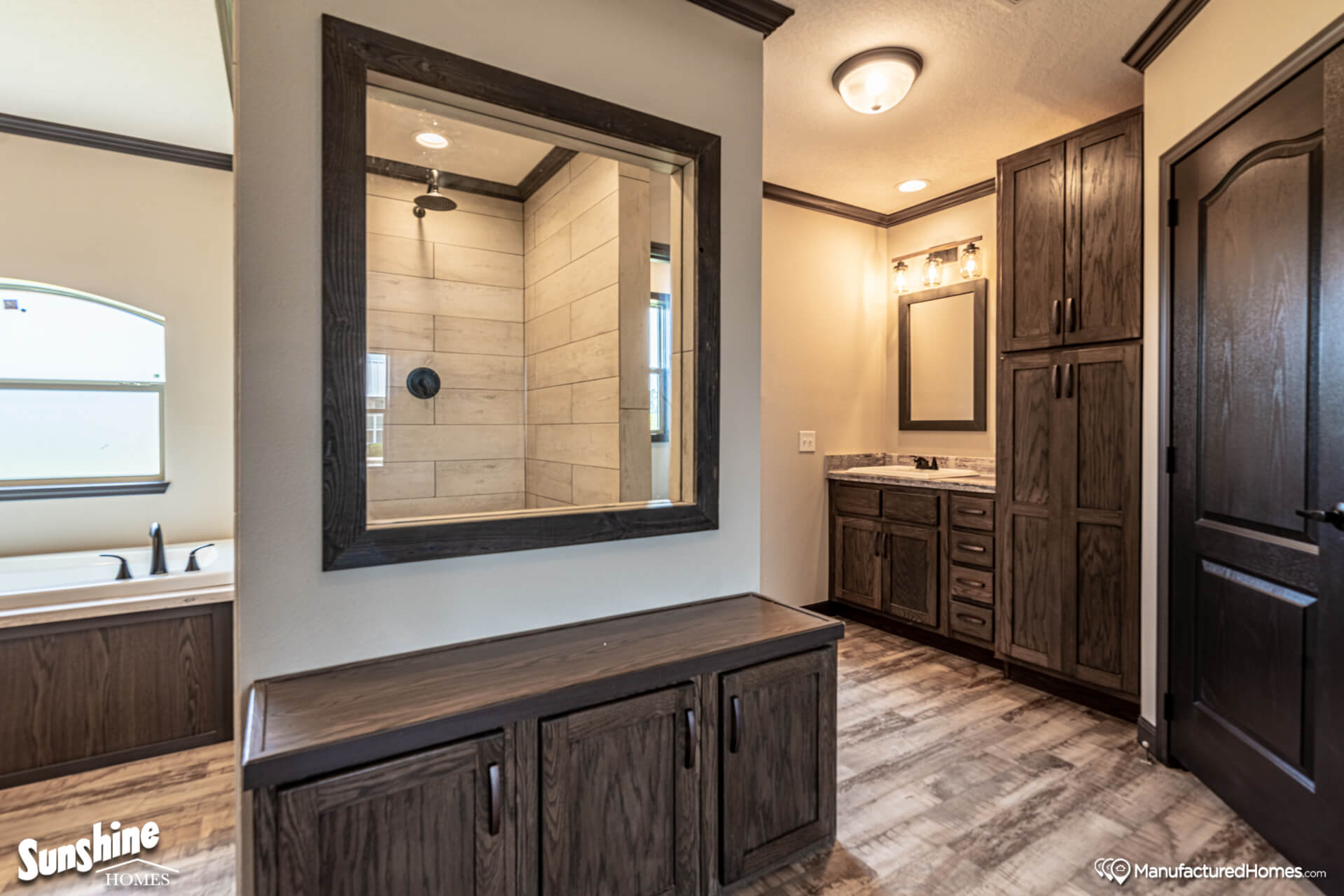 Modern bathroom with wood paneling and flooring. Features a large mirror, tiled shower, sink with vanity, and plenty of cabinet storage. Cozy ambiance.