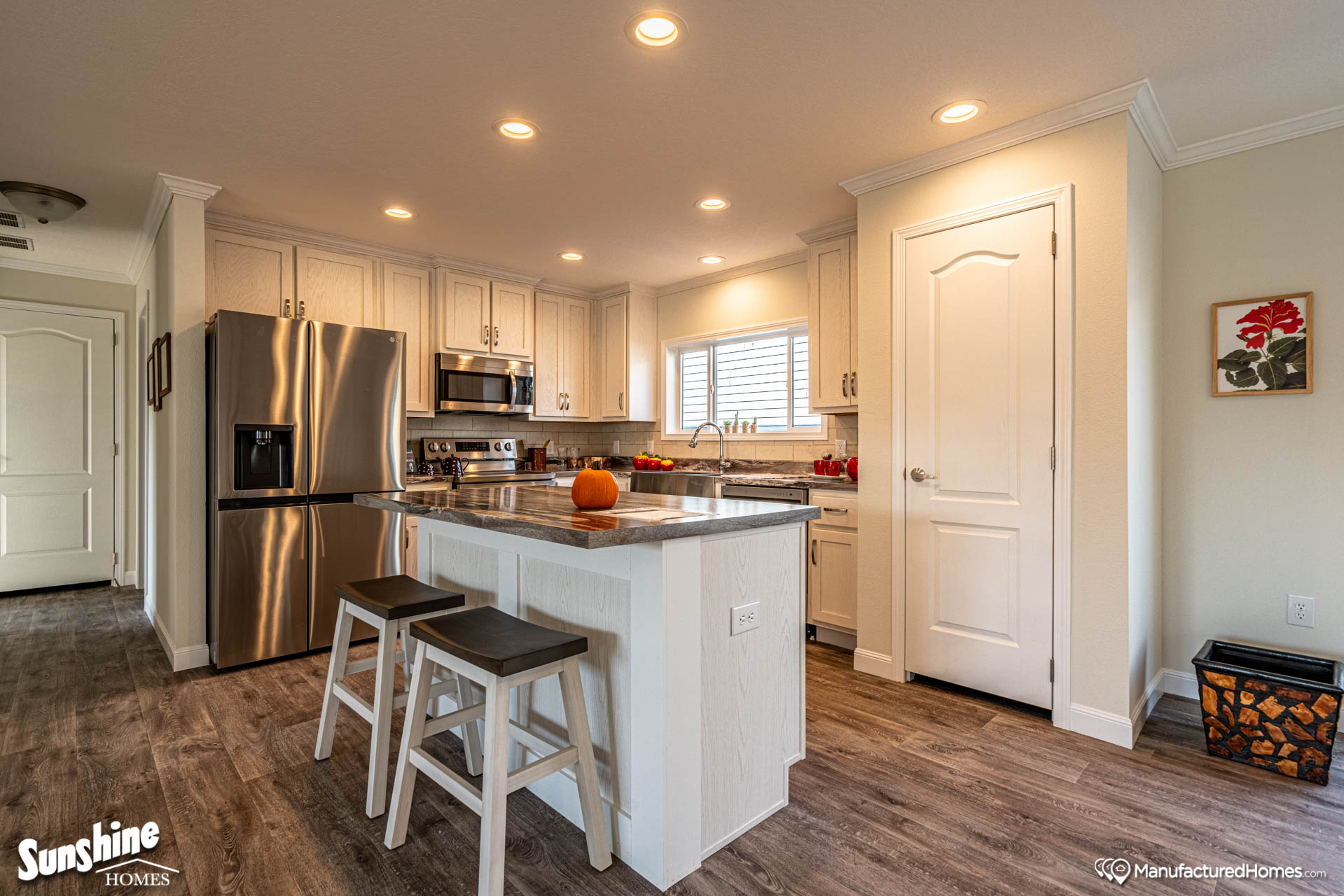 Spacious kitchen with white cabinets, a stainless steel fridge, and an island with two stools. A pumpkin adds a warm, inviting touch.
