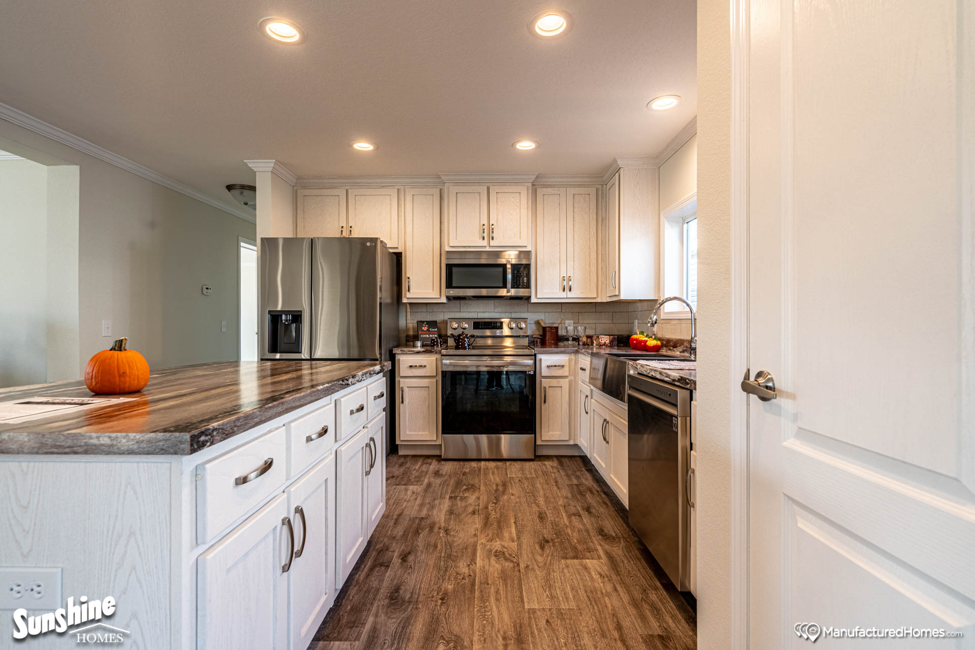 Modern kitchen with white cabinets, stainless steel appliances, wood flooring, and granite countertops. A small pumpkin adds a warm touch.