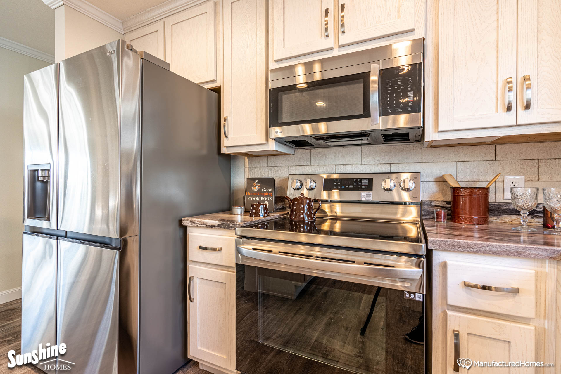 Modern kitchen with stainless steel fridge and oven, light wood cabinets, and brown countertops. A cookbook and utensils add a cozy touch.