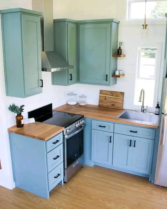 A modern kitchen with light blue cabinets, wooden countertops, and stainless steel appliances. The room is bright with a minimalist, cozy feel.