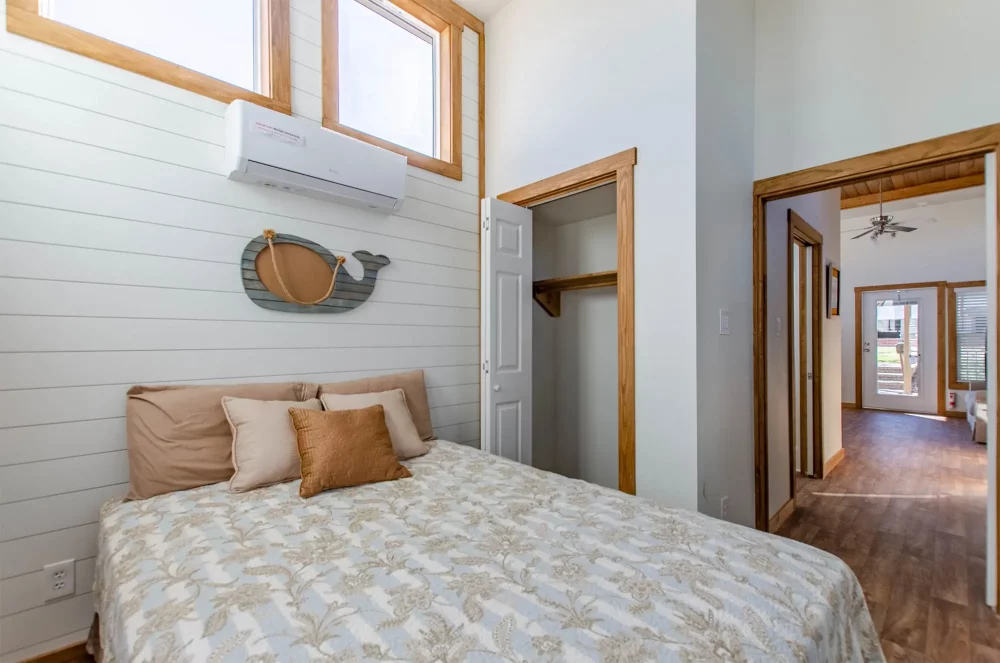 Bright bedroom with a patterned bedspread, pillows, and a decorative whale-shaped wall piece. An open closet is on the right, leading to a hallway.