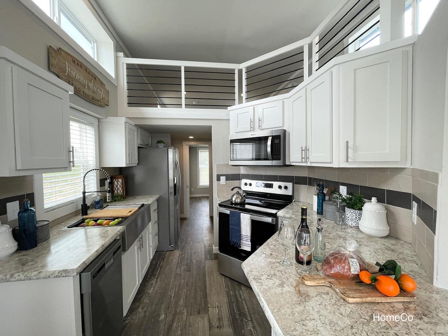 Modern kitchen with white cabinets, stainless steel appliances, and wooden flooring. Countertops hold a cutting board with vegetables and a loaf of bread, creating a cozy and inviting atmosphere.