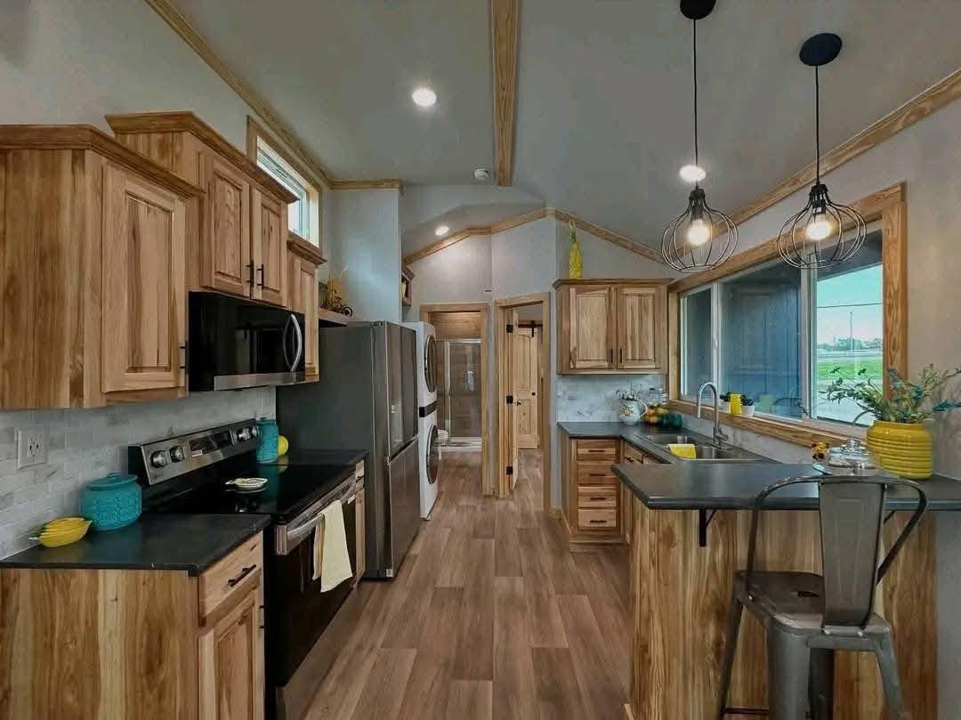 Modern kitchen with wood cabinets, stainless steel appliances, and black countertops. Pendant lights, bright yellow and teal accents add warmth.
