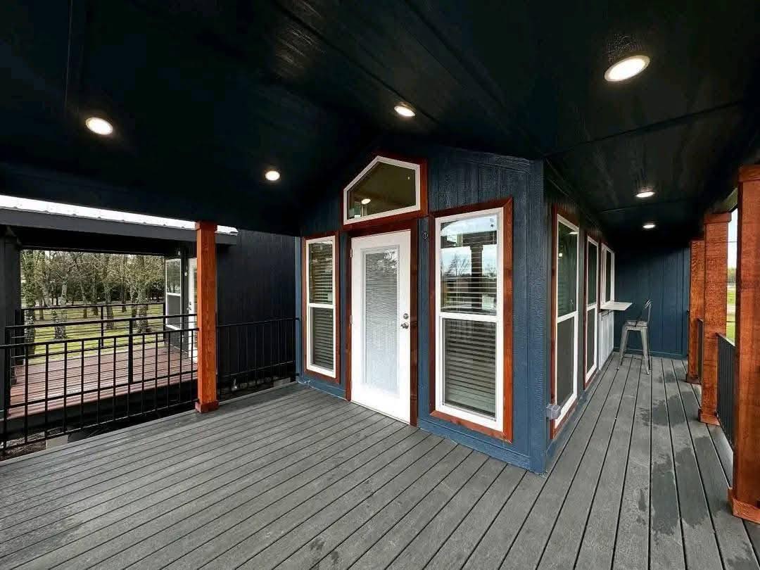 Covered porch with gray wooden floor and dark blue walls. White-framed door and windows, recessed lights, modern and inviting atmosphere.