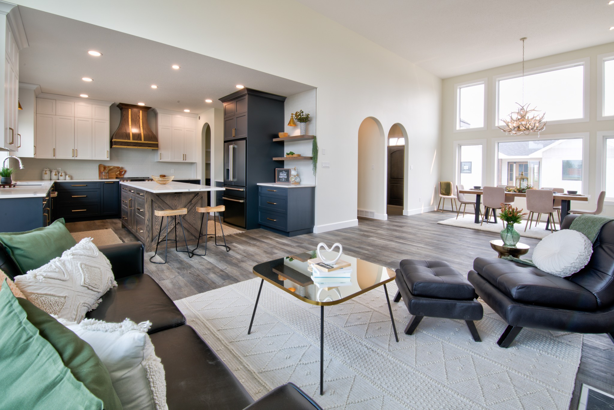 Bright, modern open-concept living room and kitchen. Features sleek furniture, large windows, dark cabinetry, and dining area with elegant lighting. Cozy and inviting.