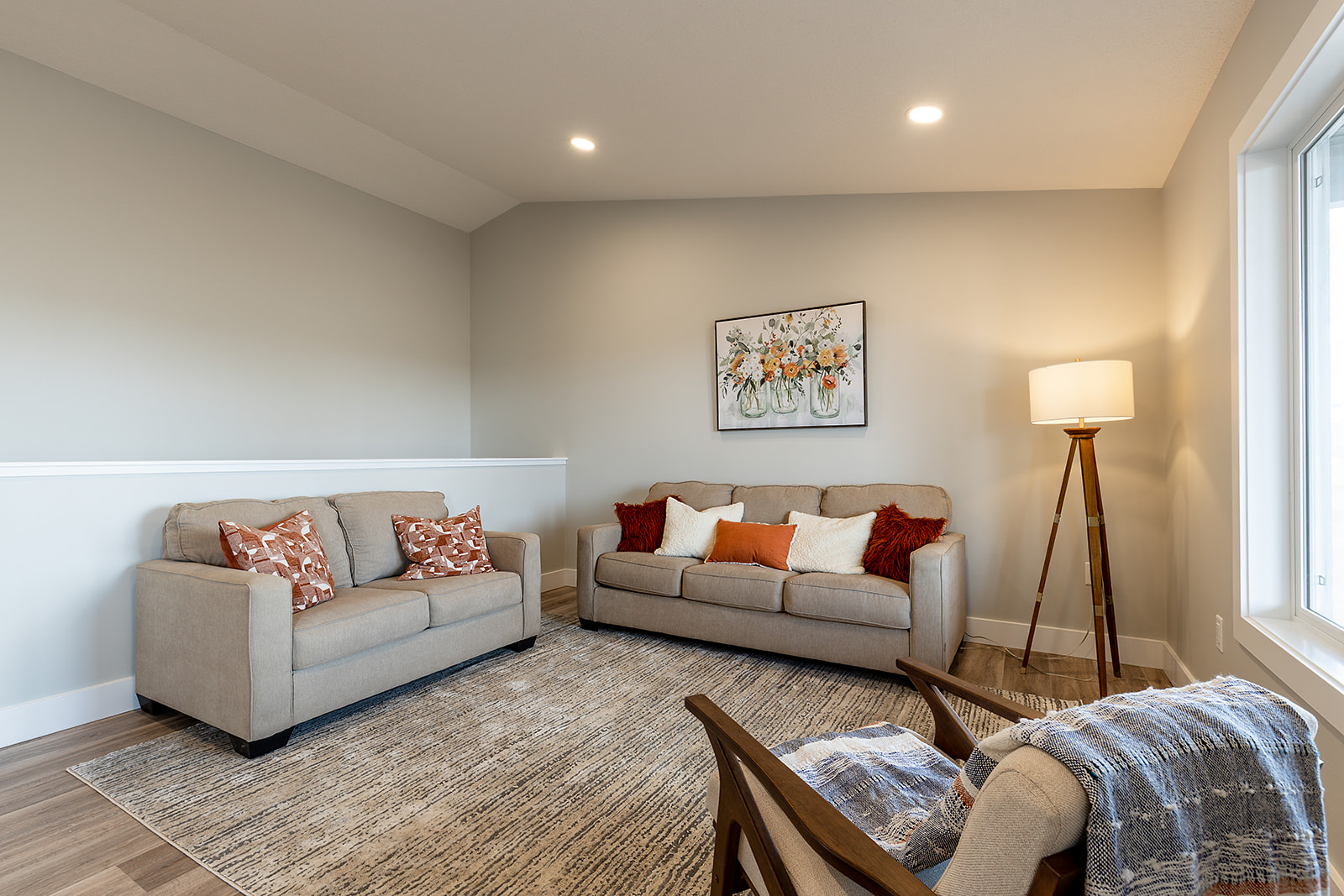Cozy living room with beige sofas adorned with vibrant cushions, artwork on the wall, a warm floor lamp, and a soft patterned rug, creating a welcoming atmosphere.
