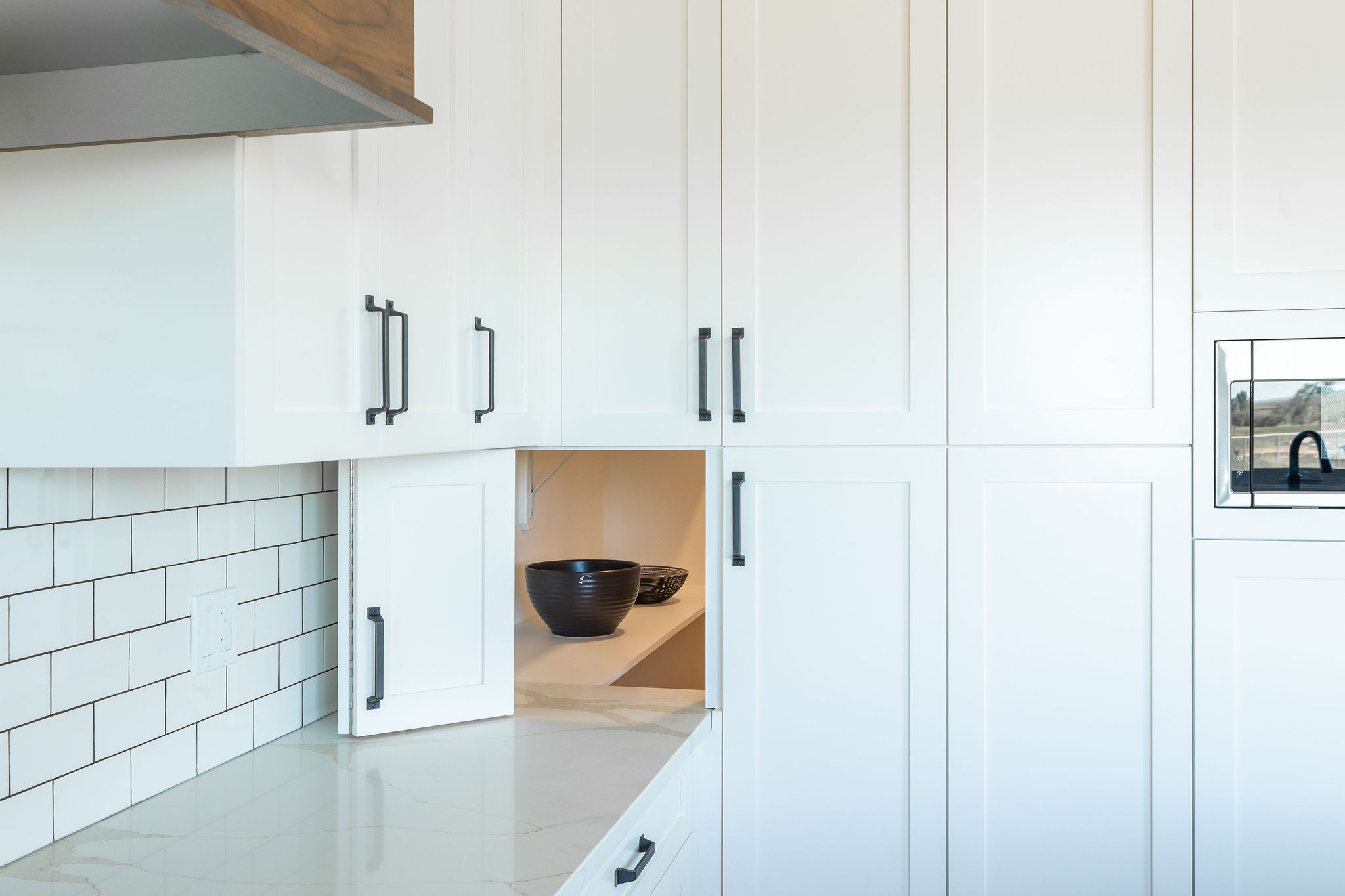 Modern kitchen with white cabinets and black handles. A cabinet door is open, revealing a black bowl inside. Clean, minimalist design.
