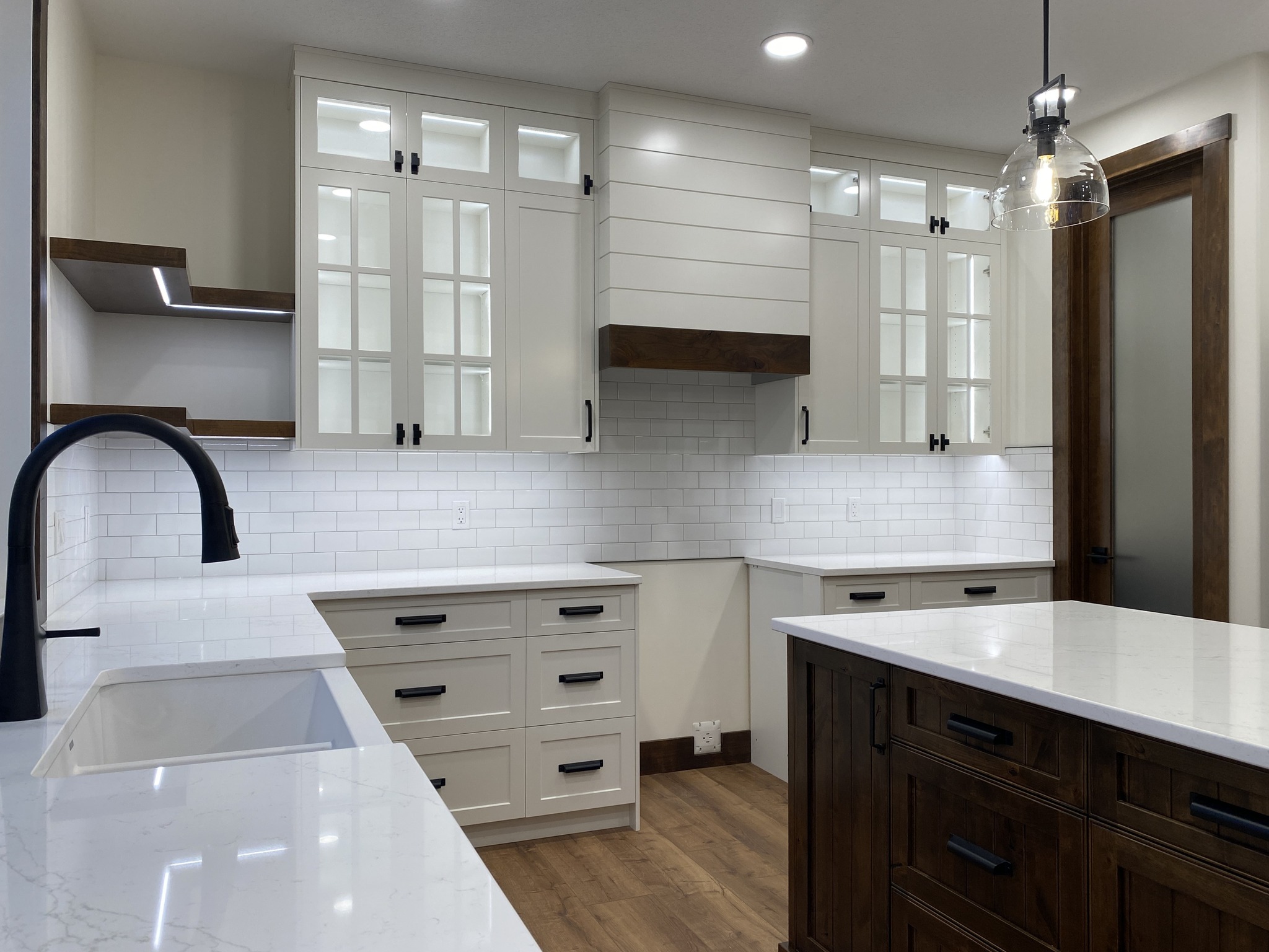Modern kitchen with white cabinets, subway tile backsplash, and dark wood accents. Features a center island, pendant light, and farmhouse sink.