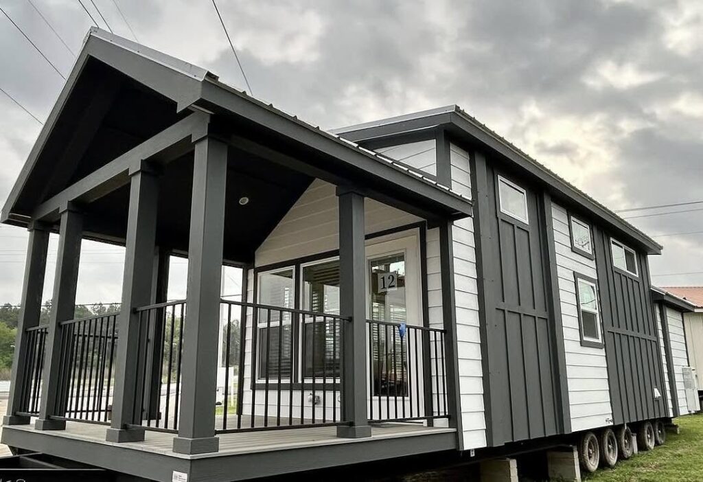 Modern tiny house on wheels with a black and white exterior and a covered porch. Cloudy sky setting adds contrast and a cozy atmosphere.