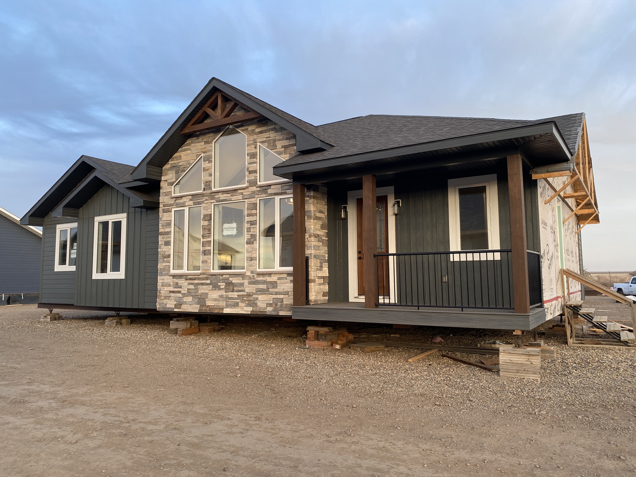 Modern house under construction on a dirt lot with brick and dark siding, large windows, and a small porch. Overcast sky in the background.