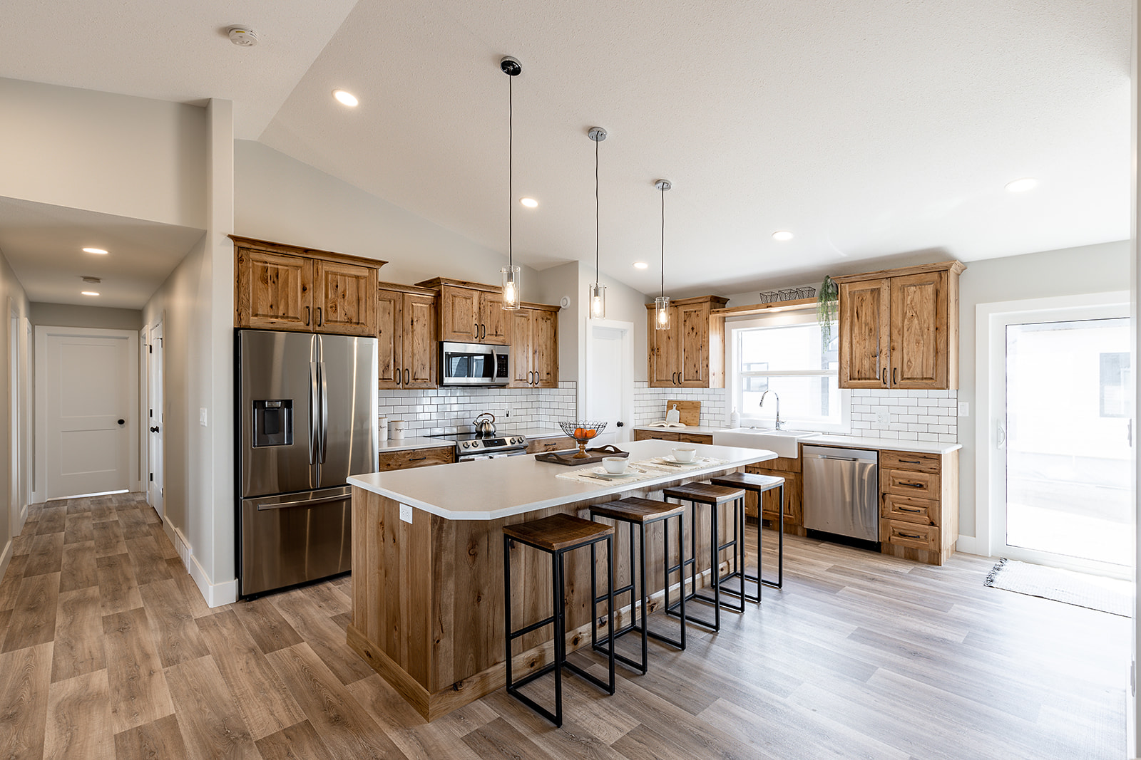 Spacious modern kitchen with wooden cabinets, stainless steel appliances, and a large central island. Bar stools, pendant lights, and hardwood floors.