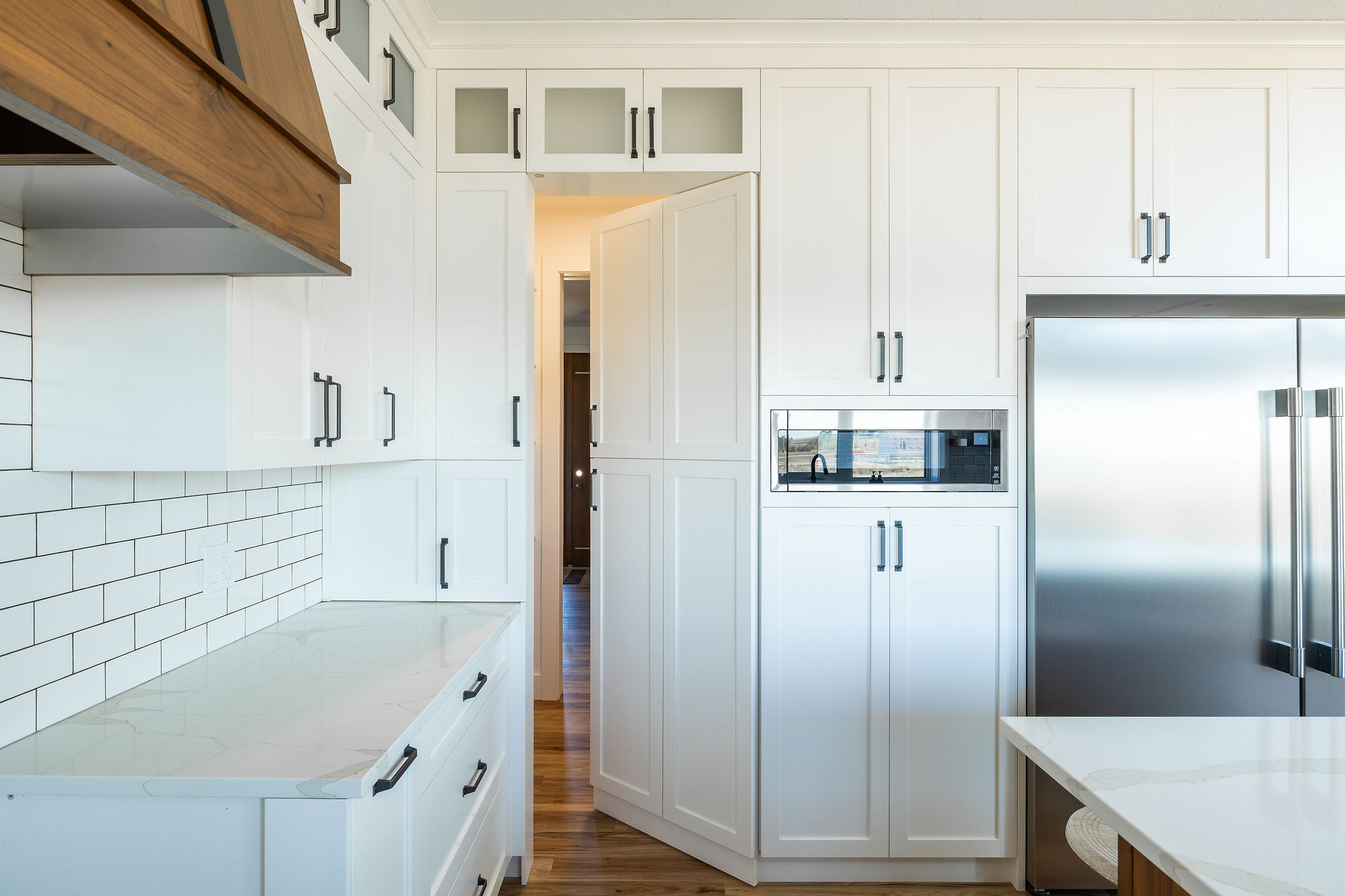 Modern kitchen with white cabinets, a stainless steel refrigerator, and minimalist décor. The wooden floor and bright lighting create a warm ambiance.