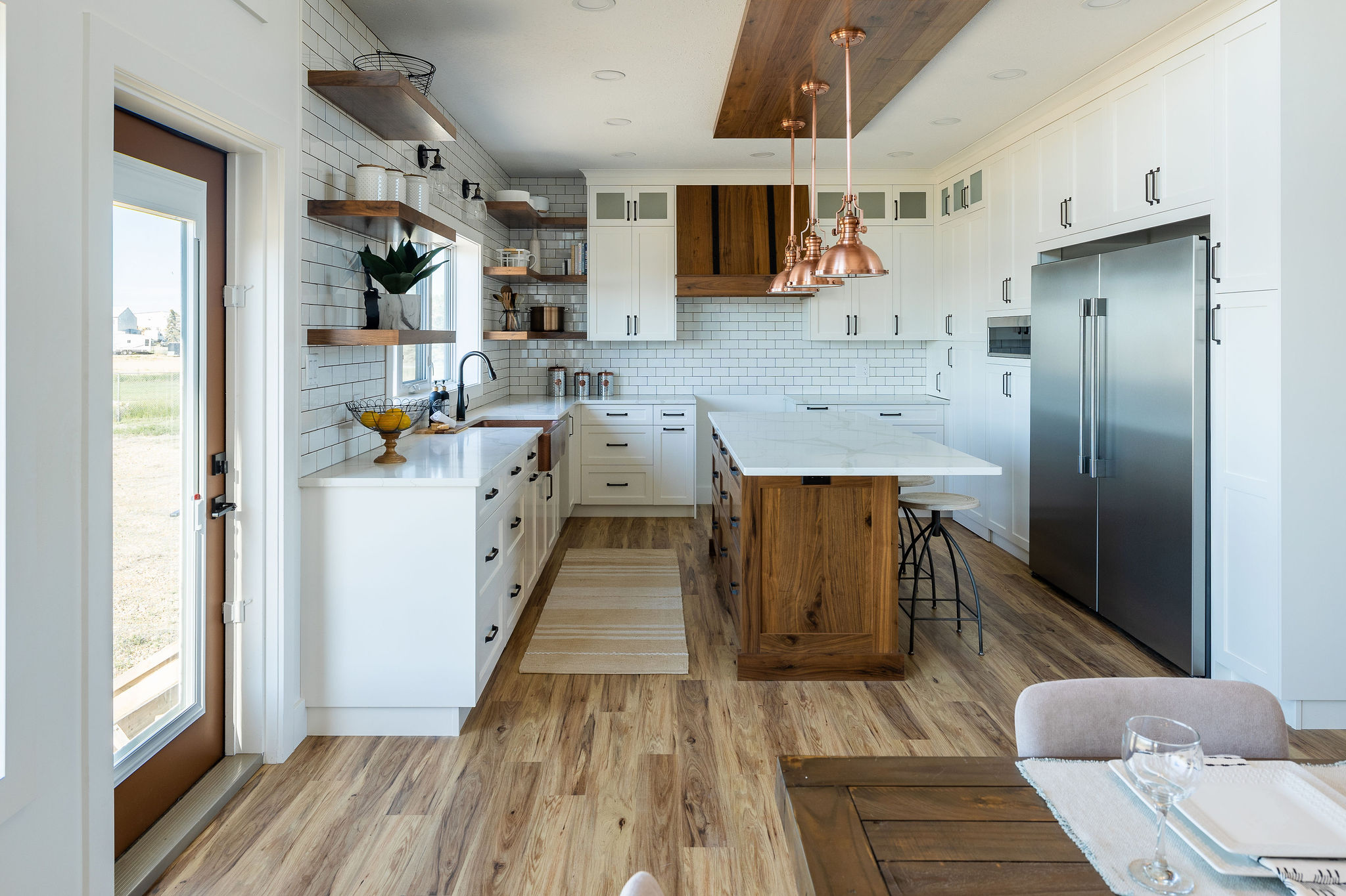 Modern kitchen with white cabinets, wooden island, and copper pendant lights. Open shelves display decor. Bright, airy ambiance with natural light.