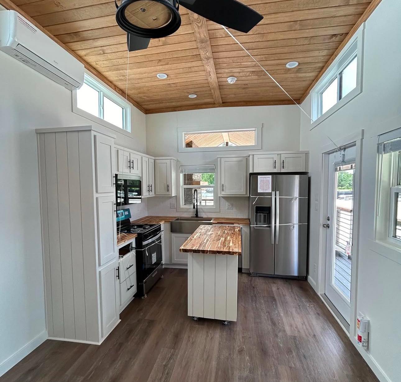 Cozy kitchen with white cabinets, wood countertops, and stainless steel appliances, under a wood-paneled ceiling with a fan. Bright and airy vibe.