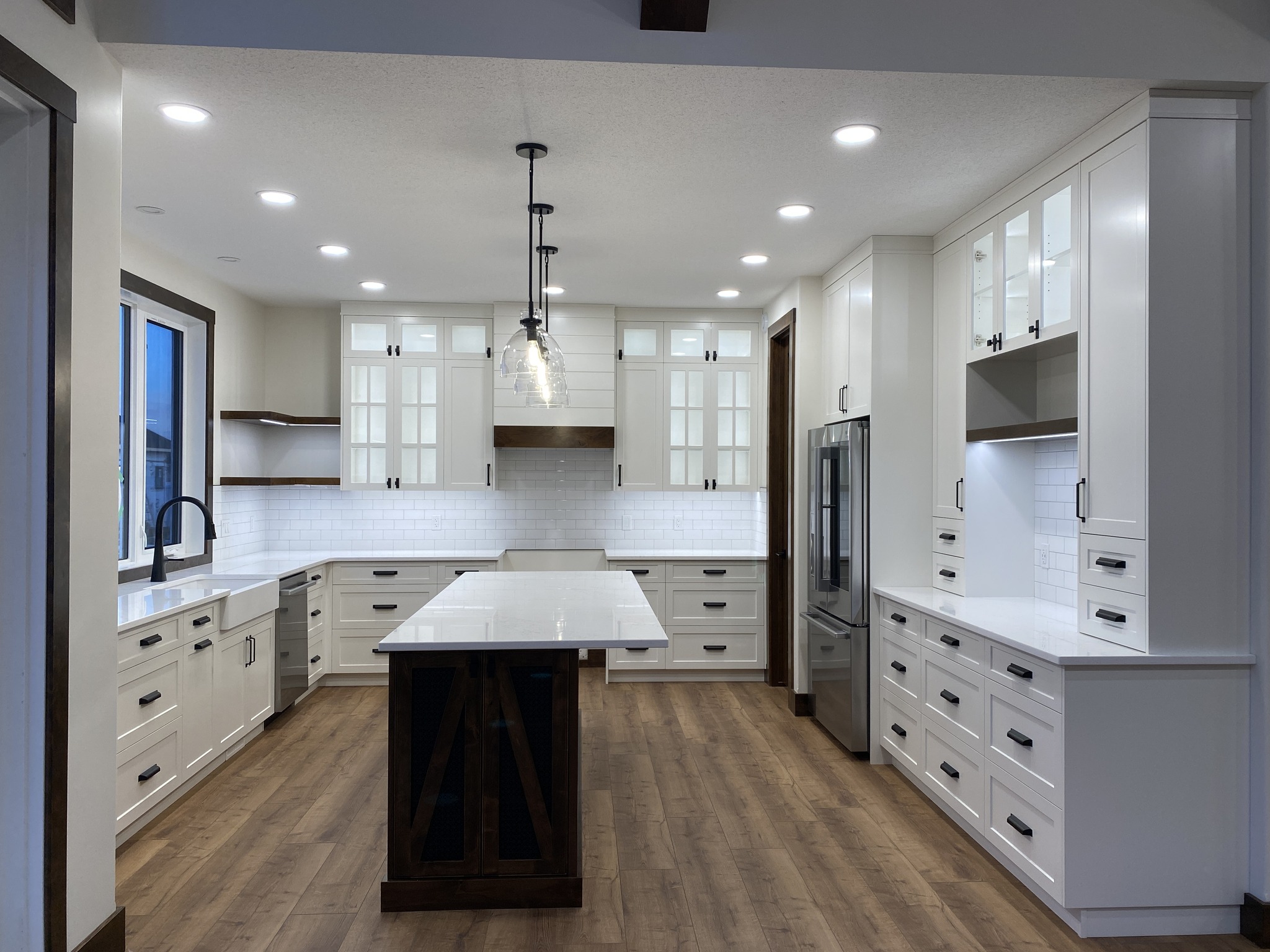 Spacious modern kitchen with white cabinets, wooden floors, and stainless steel appliances. A large island with pendant lights creates a welcoming ambiance.