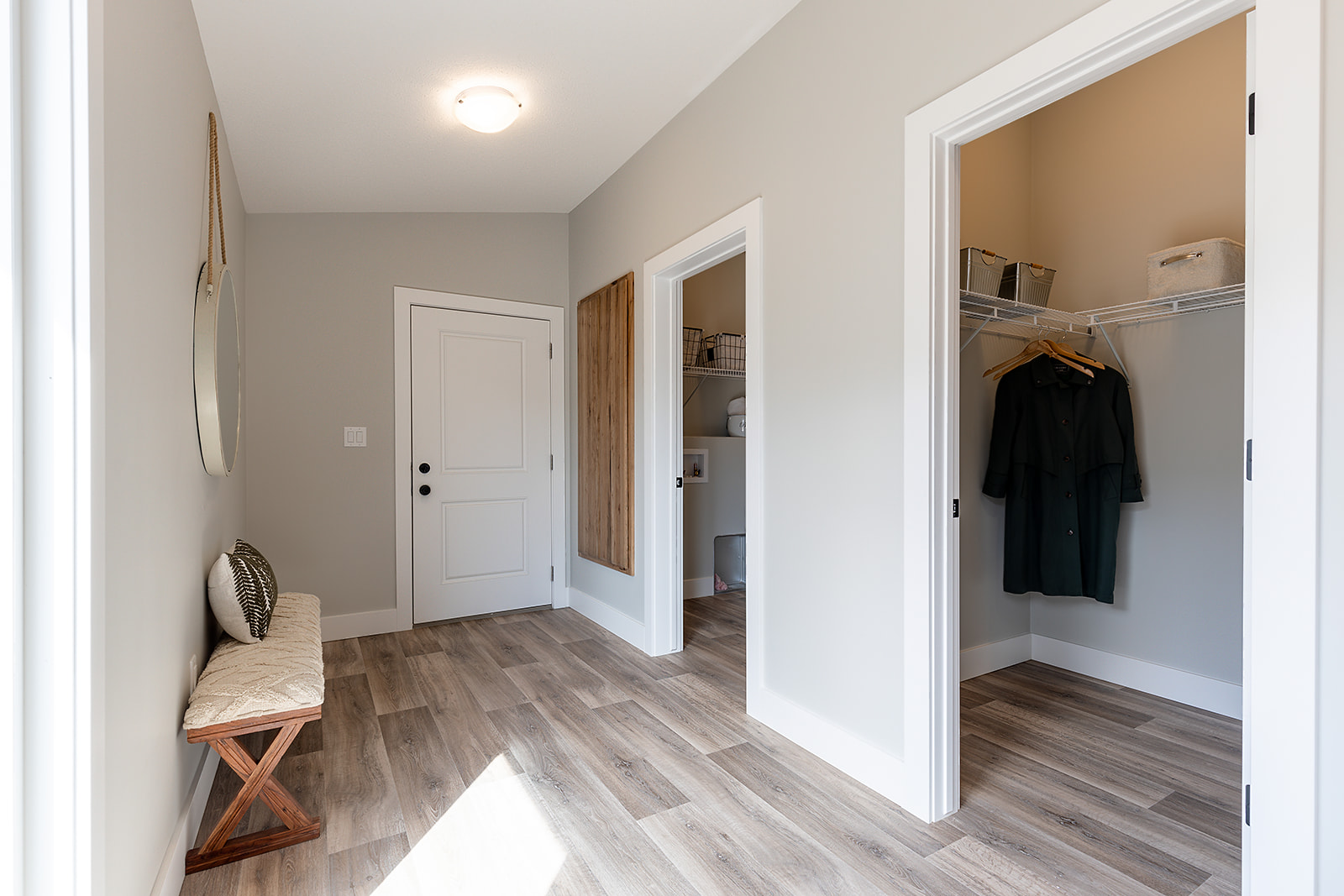 Bright hallway with light wood flooring, a cushioned bench, and two open closets. One closet has wire shelves with storage baskets, conveying a tidy, modern home.