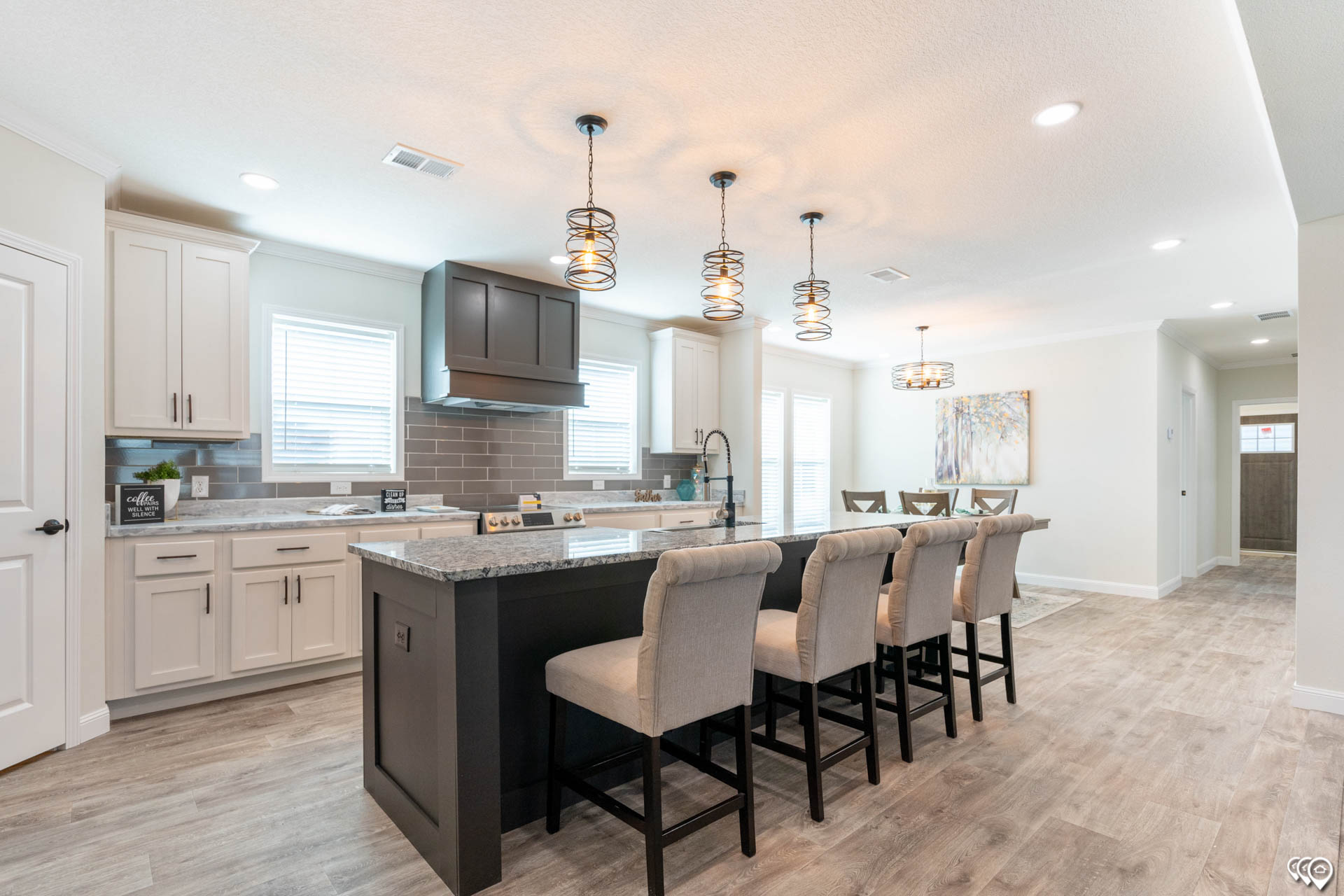 Spacious kitchen with a modern design featuring a large island with four cushioned stools, pendant lights, white cabinets, and stainless steel appliances.