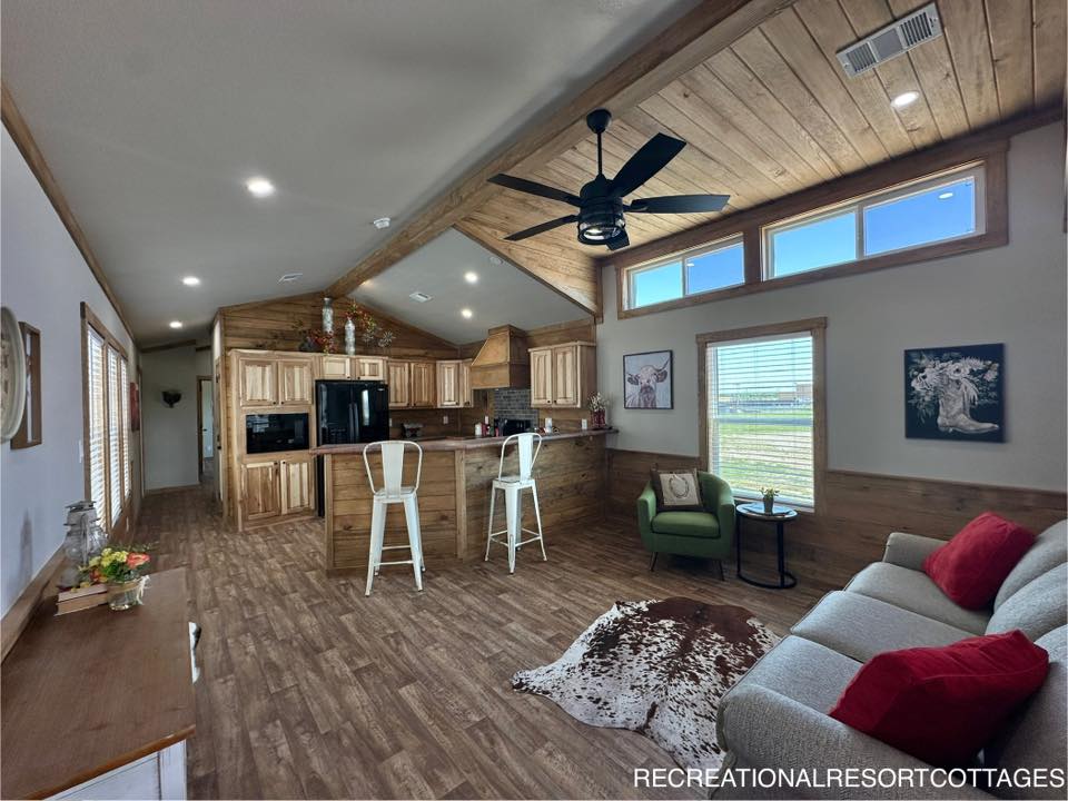 Spacious rustic kitchen and living area with wooden ceiling and floors. Features a central island with stools, a cowhide rug, and cozy seating.