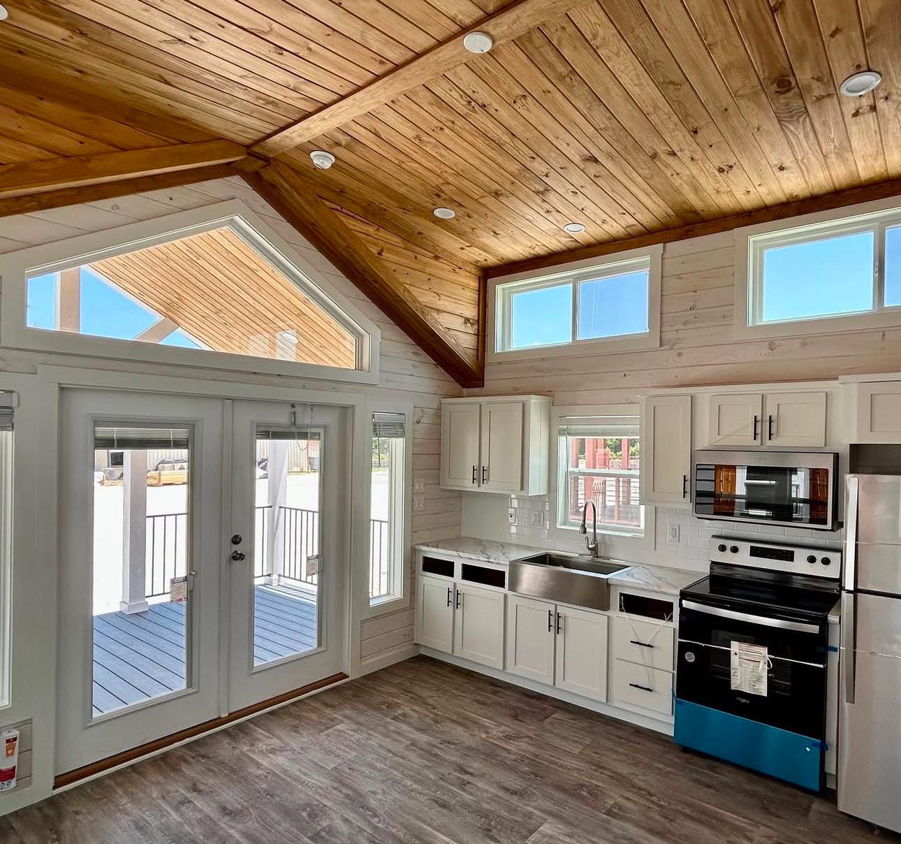 Rustic kitchen with wooden vaulted ceiling, French doors leading to the porch, white cabinets, stainless steel appliances, and light wood flooring.