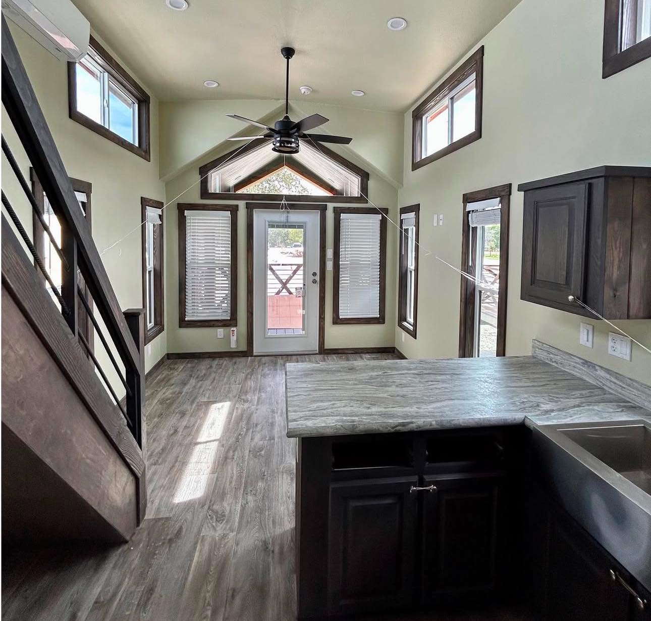 Stylish tiny home interior with high ceilings, large windows, and wooden floor. Modern staircase and sleek countertop create an airy and inviting atmosphere.