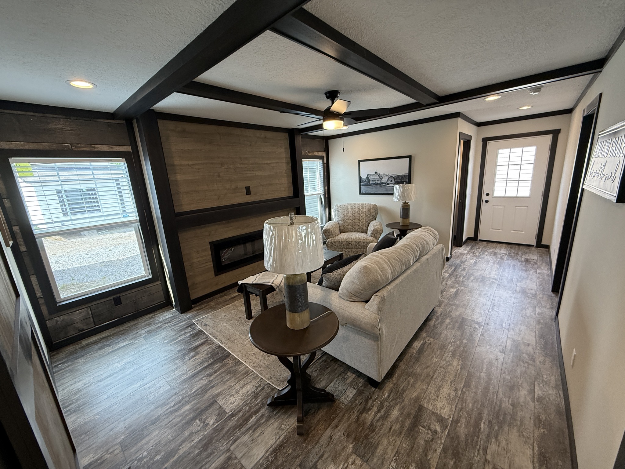 Cozy living room with wood accents, featuring a beige sofa, two armchairs, and a coffee table. A large window brightens the space, creating a welcoming atmosphere.