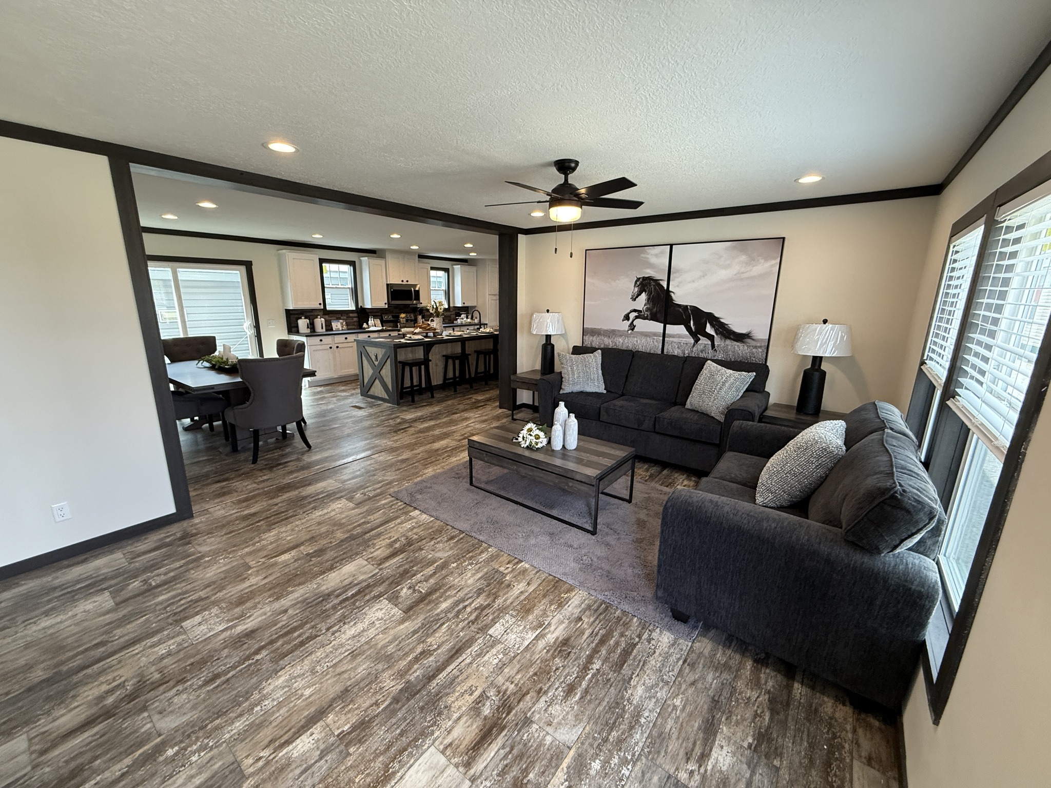 Spacious living room with dark gray sofas and a horse painting on the wall. Open concept leads to kitchen and dining area with elegant decor.
