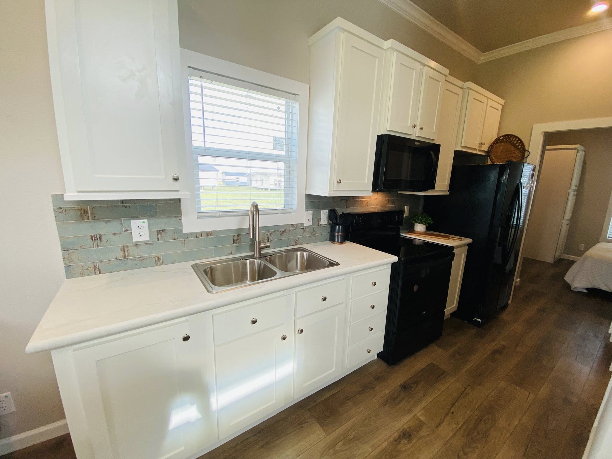 Bright kitchen with white cabinets, a double sink, and a window above. Black appliances contrast the light wood flooring, creating a cozy, inviting space.