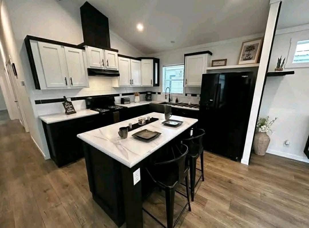 Modern kitchen with a black and white theme featuring a marble island, two black chairs, wooden floor, and black appliances. A cozy, stylish space.