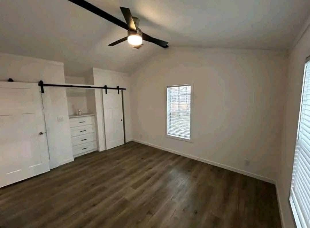 Spacious, empty room with light walls and hardwood floor. Ceiling fan with light in the center, a window on the right, and a closet with sliding doors on the left.