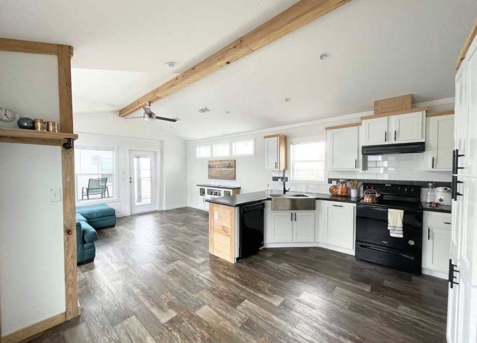 Modern kitchen with a vaulted ceiling features white cabinets, black appliances, a wooden island, and hardwood floors. A teal sofa and patio doors are on the left. Cozy and spacious.