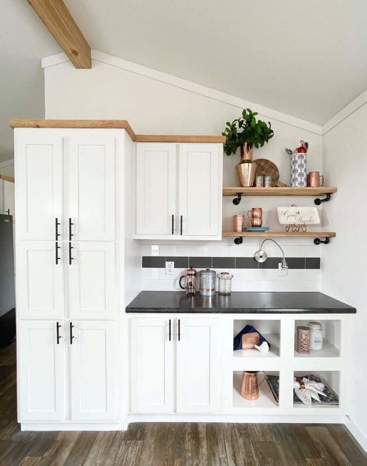 Modern kitchen nook with white cabinets and wooden accents. Features open shelves with potted plant, copper accessories, and a black countertop.