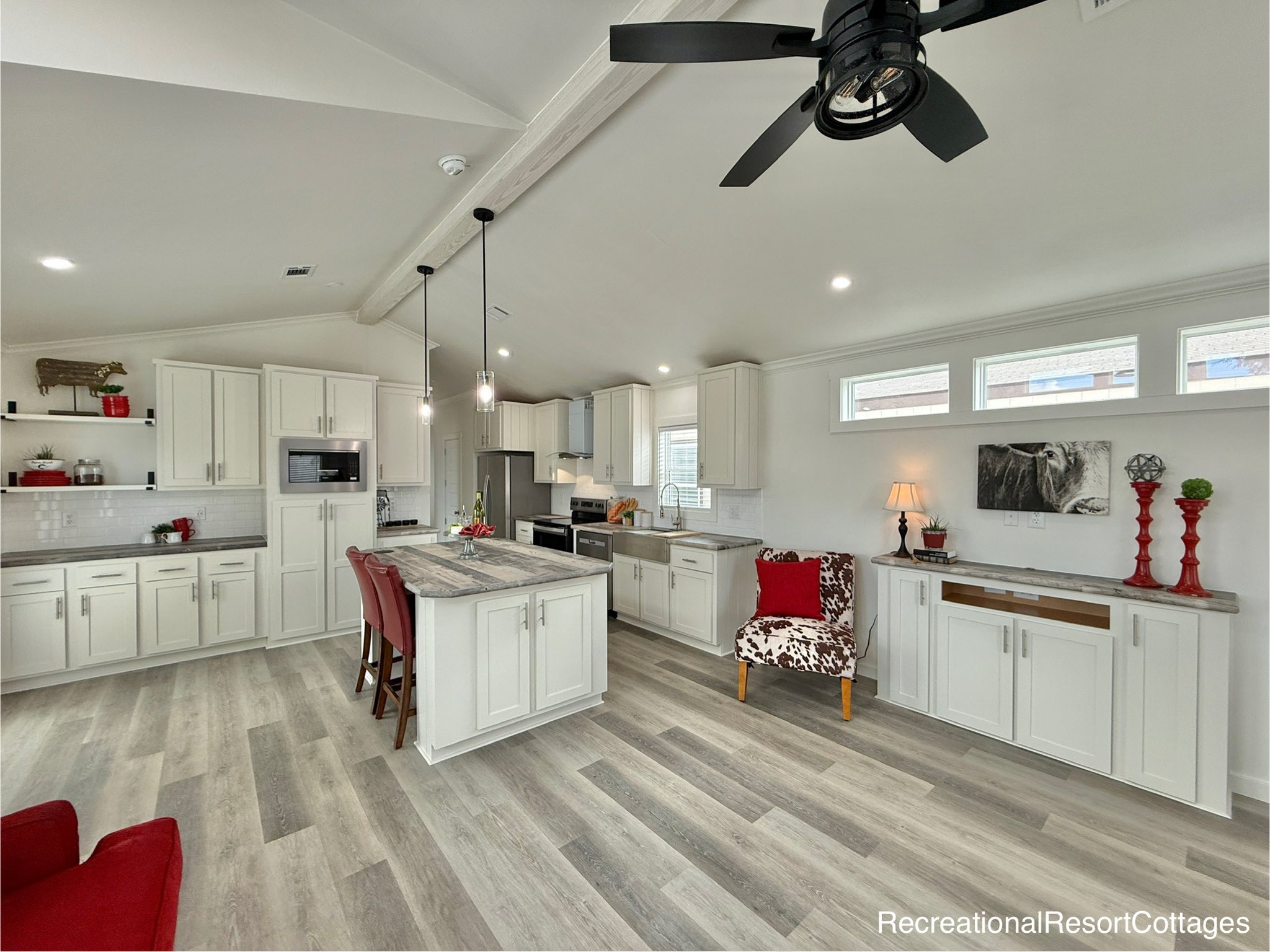 Modern kitchen and living area with white cabinets, island, and gray countertops. Red accents, decorative items, and a cozy ambiance with soft lighting.