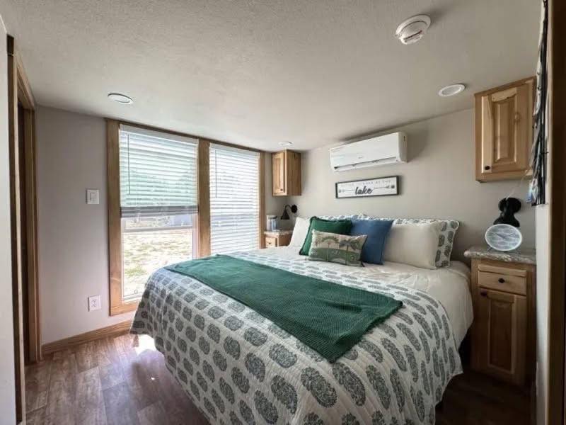 Cozy bedroom with large windows and a nature view. Bed with green and blue accents, wood cabinets, and modern decor creating a tranquil ambiance.
