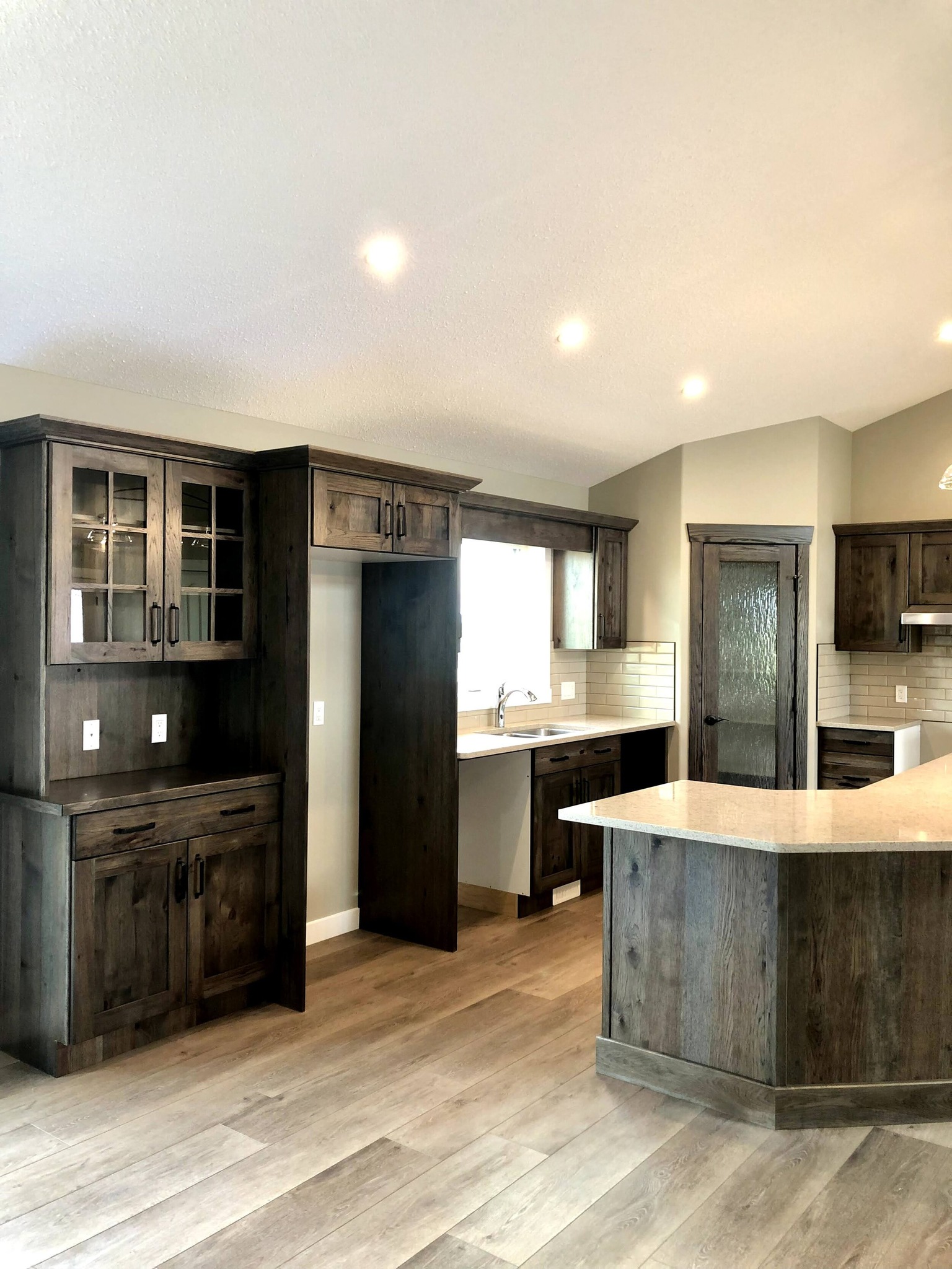 Spacious kitchen with dark wood cabinets, light countertops, and a central island. Soft lighting creates a warm, inviting atmosphere.