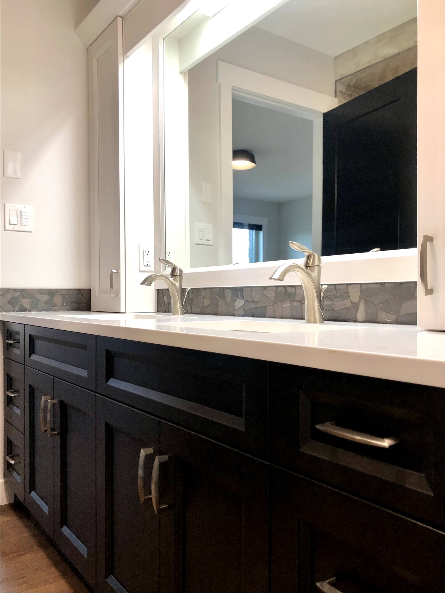 Sleek bathroom vanity with two stainless steel faucets, large mirrors, black cabinets, and mosaic tile backsplash, conveying a modern, elegant style.