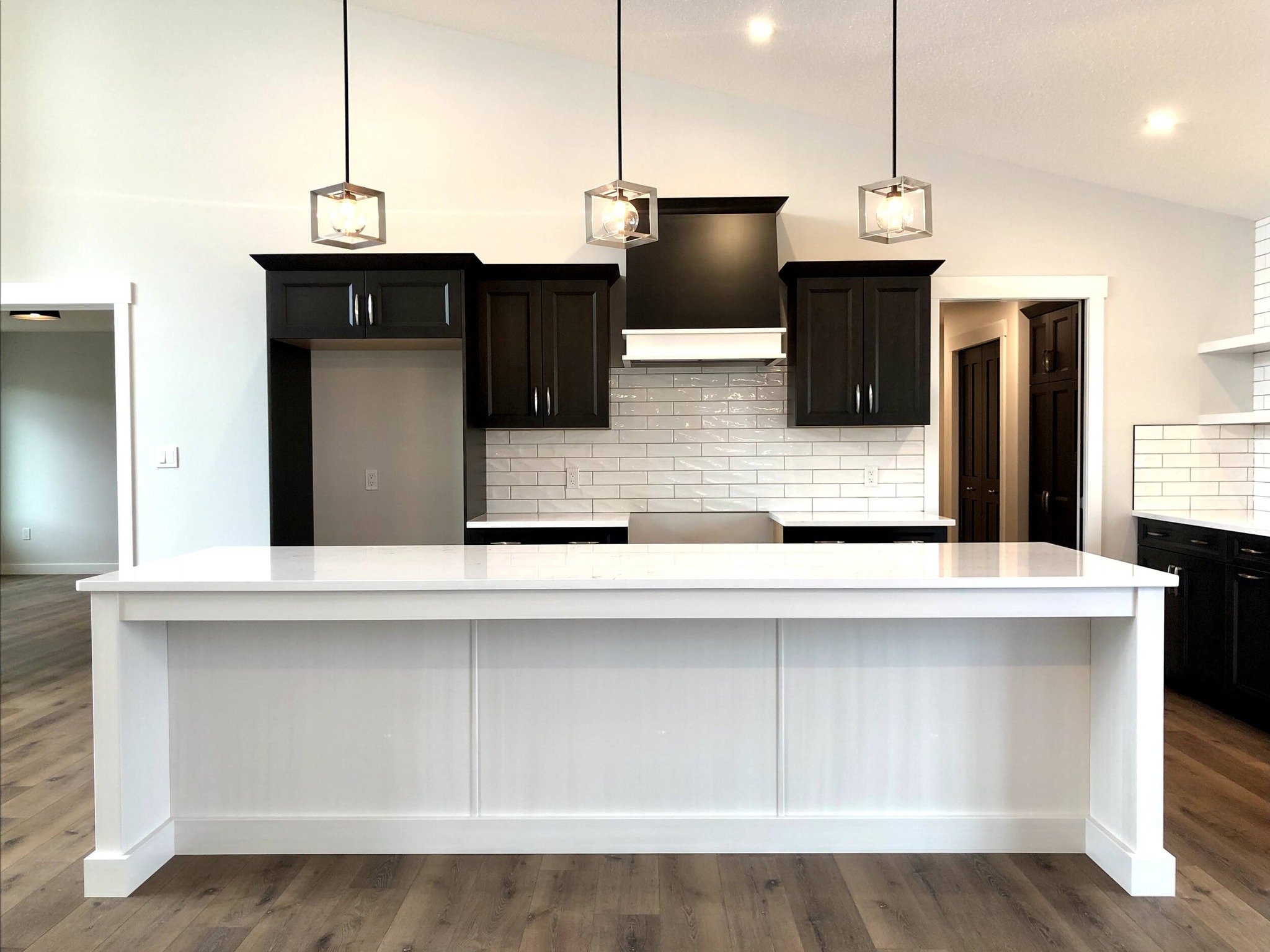 Modern kitchen with a white island and countertop, dark cabinets, and subway tile backsplash. Three pendant lights hang above, creating a clean, sleek look.
