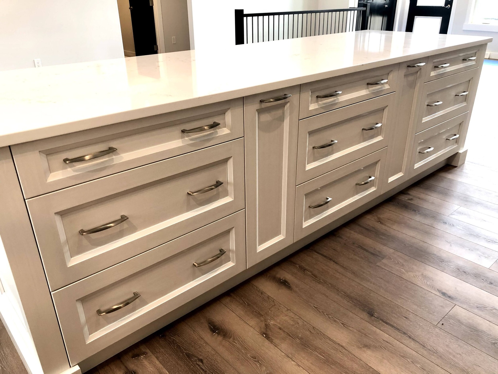 White kitchen island with multiple drawers and silver handles on a wooden floor. The sleek design and neutral tones create a modern, clean aesthetic.