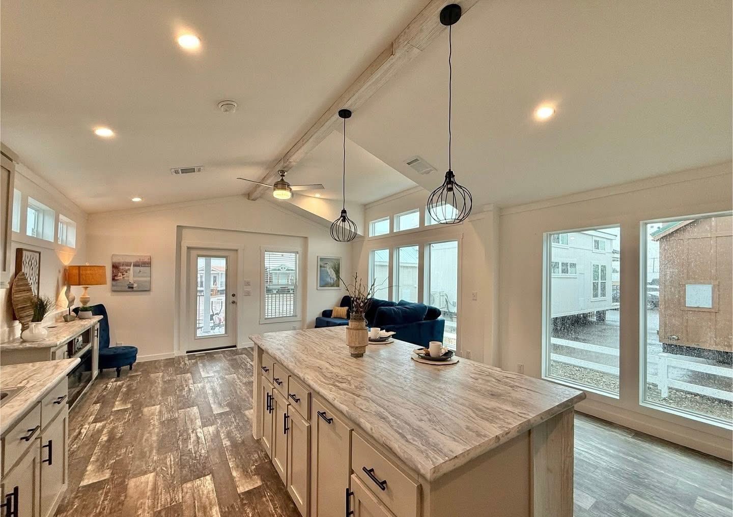 Spacious, modern kitchen with a large marble island, pendant lights, and wood flooring. The room feels bright and airy with large windows and a cozy seating area.