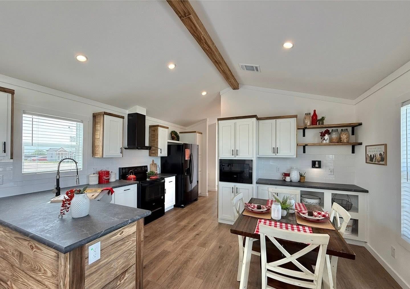 Bright kitchen and dining area with wooden floors, white cabinets, and black appliances. A small table is set for two, evoking a cozy, welcoming feel.