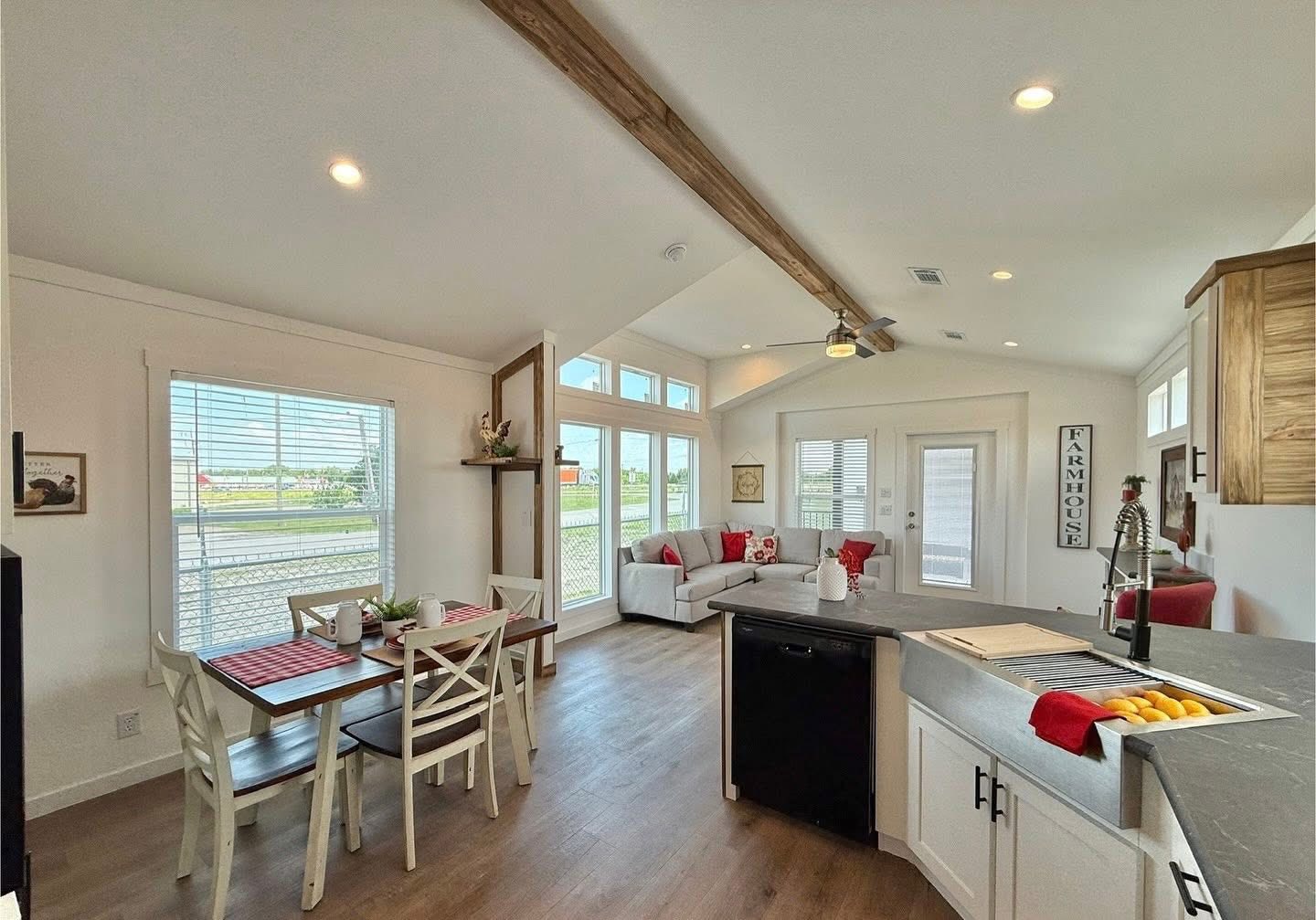 Bright, modern farmhouse interior with high ceiling and wooden beam. Open layout includes a dining area, cozy living space, and a sleek kitchen.