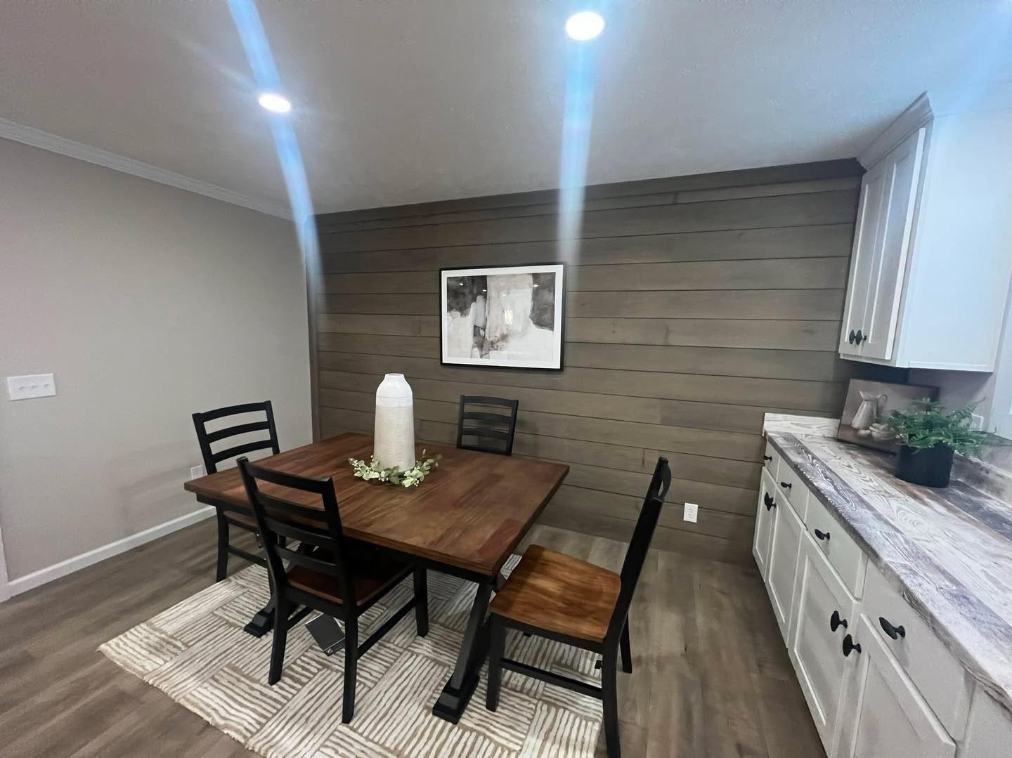 Dining area features a wooden table with four chairs, a white vase centerpiece, and abstract wall art. The space is modern with a cozy feel.