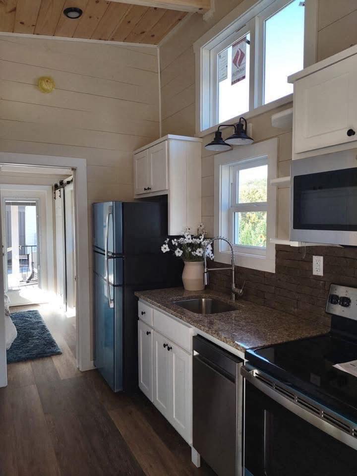 A modern kitchen with wood floors and white cabinets. Features a stainless steel refrigerator, oven, and microwave. Vase with flowers on granite countertop.
