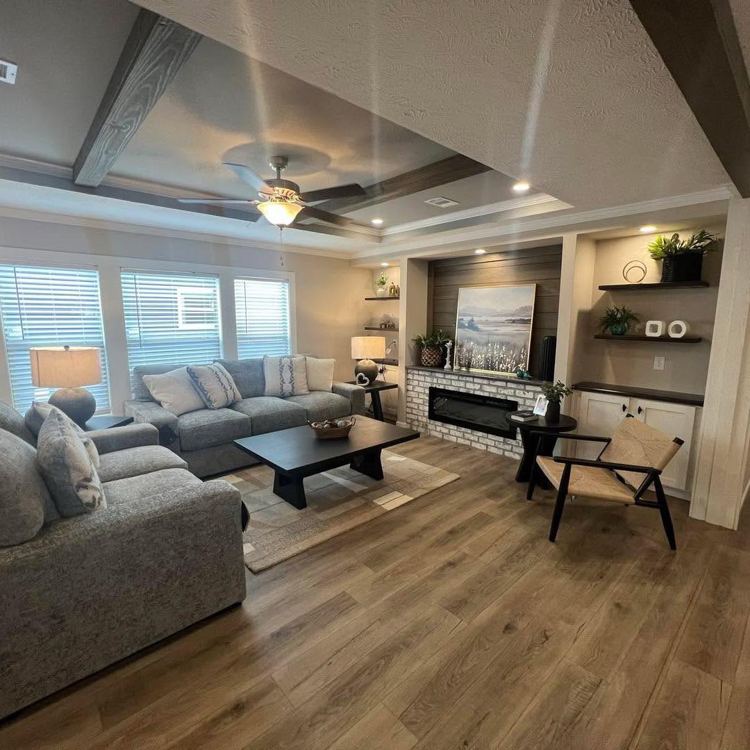Stylish living room with a gray sectional sofa, wooden coffee table, and modern decor. Features a fireplace, wall art, and ceiling fan, creating a cozy ambiance.