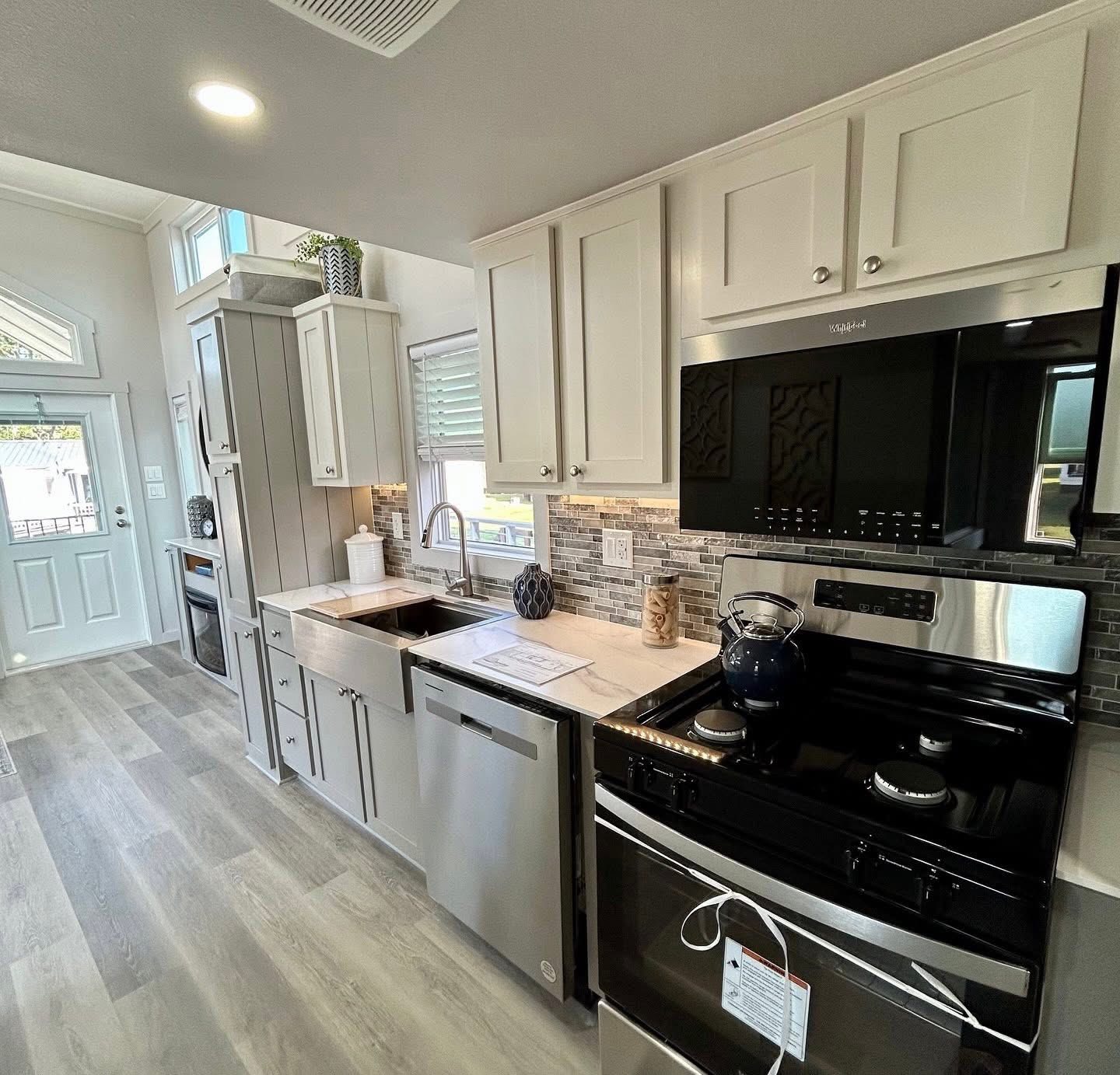 Modern kitchen with light wood flooring, white cabinets, stainless steel appliances, and mosaic tile backsplash. Bright, airy, and sleek ambiance.