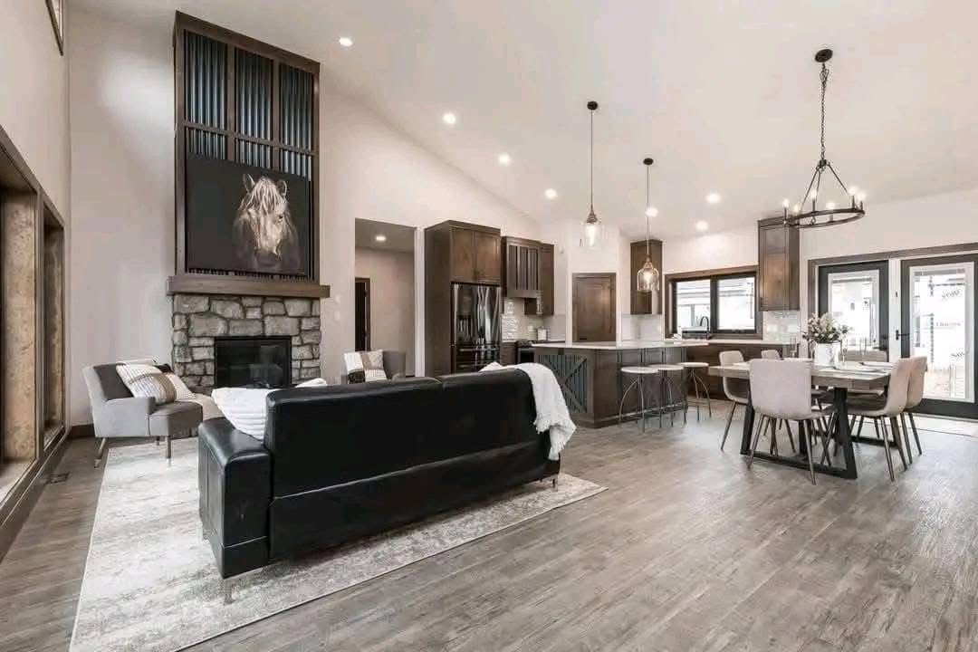 Modern open-concept living room and kitchen with high ceilings, featuring a black sofa, stone fireplace with lion artwork, and elegant dining area.
